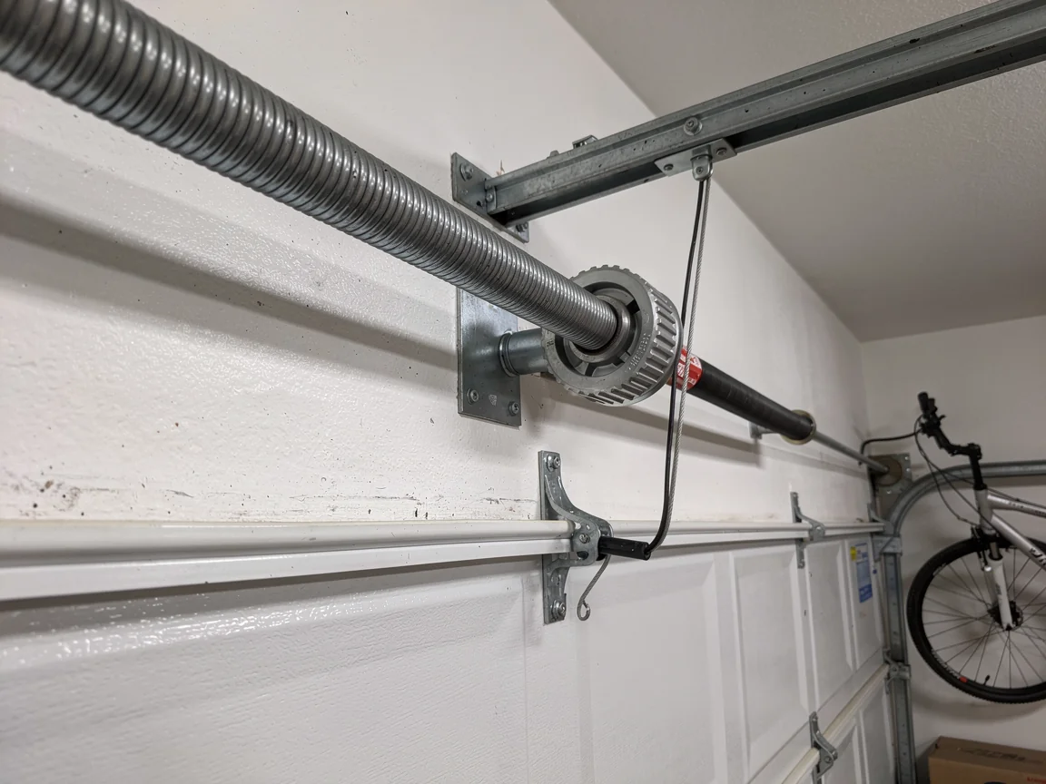 A garage door torsion spring is mounted above a white garage door.